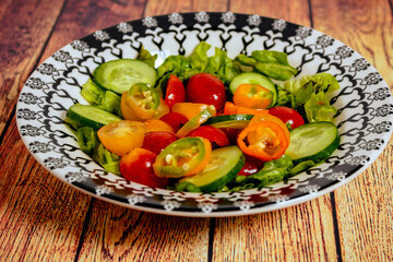 Fresh two-color cherry tomato salad, lettuce, red onion and hot chili served in a vintage bowl on a table. 45 deg. view. close-up.