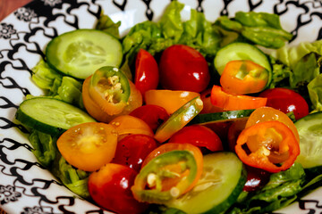 Fototapeta na wymiar Fresh two-color cherry tomato salad, lettuce, red onion and hot chili served in a vintage bowl on a table. 45 deg. view. close-up.