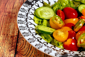 Fresh two-color cherry tomato salad, lettuce, red onion and hot chili served in a vintage bowl on a table. 45 deg. view. close-up.