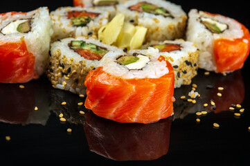 Traditional sushi with sesame seeds - Philadelphia with salmon, avocado and cheese. Japanese cuisine on black background