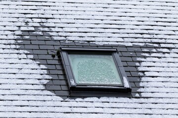 A vertical portrait of a frozen slate roof with a tiltable skylight window which is also frozen...