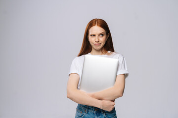 Frustrated upset young business woman or student holding laptop computer and looking away on isolated gray background. Pretty lady model with red hair emotionally showing facial expressions.