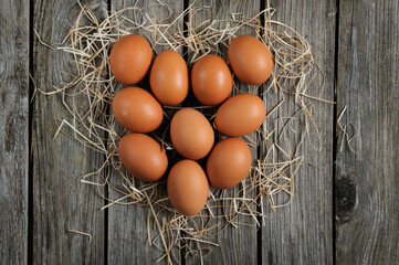 Top view of raw eggs laid out in heart shape with hay on wooden background