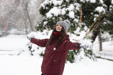 Fototapeta premium Portrait of a white young woman with everything snowy, wears a red coat and a gray hat. It's snowing. Is throwing a snowball