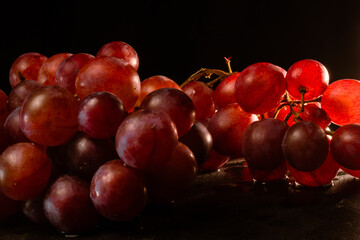 Close-up of bunches of red grapes on a black slab. Intimate lighting. Concept delicacy, purity of the product.