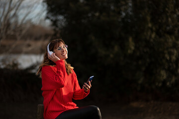 Mujer joven escuchando música con auriculares en parque.