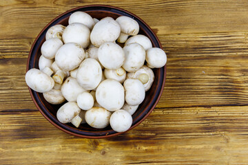 Fresh champignon mushrooms in ceramic bowl on the wooden table. Top view