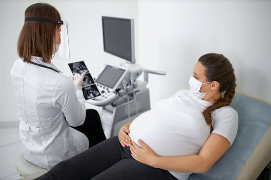 Doctor in mask showing pregnant woman ultrasound images