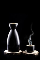Sake, a traditional distilled and fermented alcoholic drink from Japan, served hot, produced from rice, water and kōji. Black background with copy space