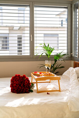 Celebrating Saint Valentine's Day with bouquet of red roses, glass of champagne and croissants on tray on bed. Romantic surprise breakfast for Mother's day or International women day