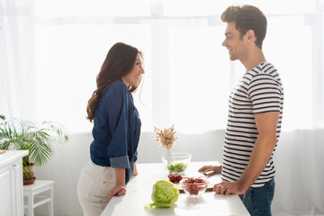 side view of happy couple looking at each other near ingredients on table