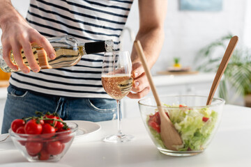 Obraz na płótnie Canvas cropped view of man pouring white wine in glass near salad