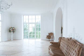 chic white huge spacious hall with a minimum of expensive antique furniture. Baroque interior design with ornament on the walls and parquet on the floor.