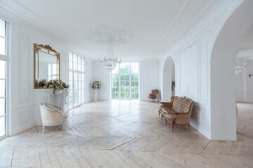 chic white huge spacious hall with a minimum of expensive antique furniture. Baroque interior design with ornament on the walls and parquet on the floor.