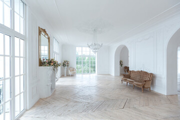 chic white huge spacious hall with a minimum of expensive antique furniture. Baroque interior design with ornament on the walls and parquet on the floor.