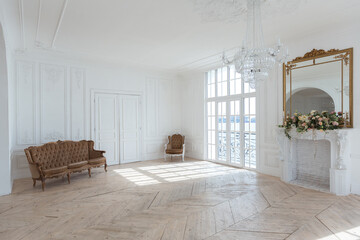 chic white huge spacious hall with a minimum of expensive antique furniture. Baroque interior design with ornament on the walls and parquet on the floor.