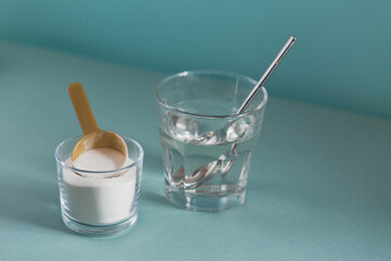 Collagen powder in bowl, glass of water and measure spoon on light blue background. Extra protein intake. Natural beauty and health supplement concept.