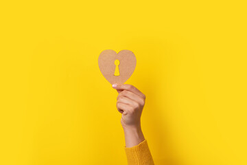 wooden heart with keyhole in hand over yellow background