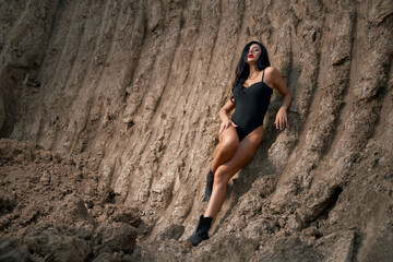 Stunning woman in black bodysuit posing in sand quarry