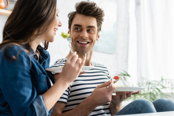cheerful man holding plate with salad and looking at girlfriend on blurred foreground