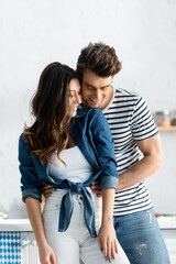 happy man embracing girlfriend and smiling in kitchen