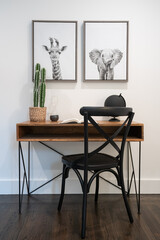 Detail of wood desk with black metal legs, black wood chair, planted cactus, and animal print art.