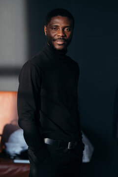 Portrait of attractive stylish african american man in black turtleneck standing in sunbeams and posing for a photo