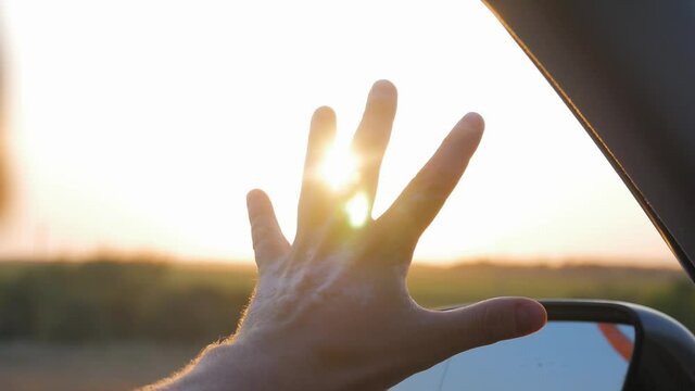 Man hand touching sunlight while traveling by car.