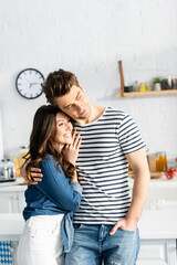 man hugging cheerful girlfriend and looking away in kitchen