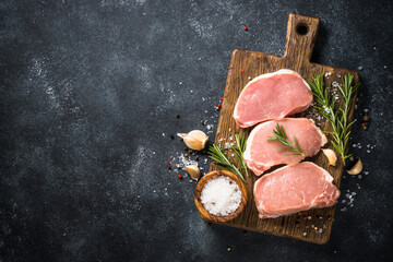 Pork meat. Fresh pork steaks on cutting board with ingredients for cooking. Top view at black stone...