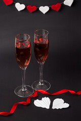 Two Champagne glasses on the black background with a red ribbon and white hearts. Composition for Valentine's day	