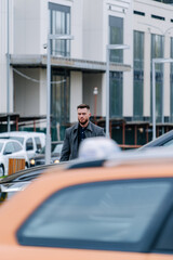 Selective focus on handsome pedestrian man in grey coat. Yellow taxi on front blurred view. Modern...