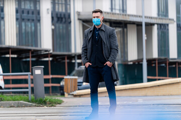 Handsome young man in coat and suit on the street with a medical face mask on. Protection against infection. Influenza virus or coronavirus.