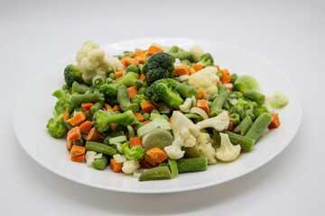Frozen vegetables: cauliflower, green peas, leeks, broccoli, carrots, green beans on a white plate.