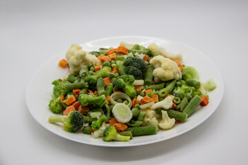 Frozen vegetables: cauliflower, green peas, leeks, broccoli, carrots, green beans on a white plate.