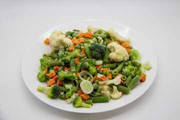 Frozen vegetables: cauliflower, green peas, leeks, broccoli, carrots, green beans on a white plate.