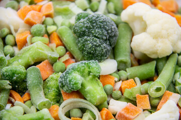 Frozen vegetables: cauliflower, green peas, leeks, broccoli, carrots, green beans on a white plate.