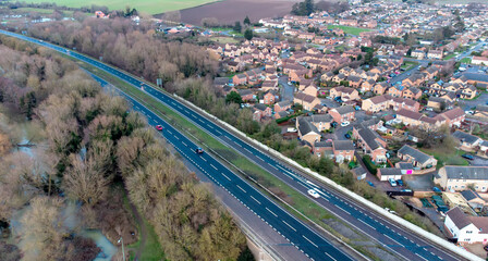 A high angle view of traffic on a dual carriageway passing next to a village in Suffolk, UK