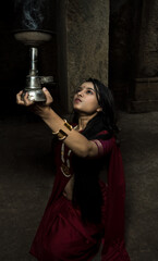 beautiful Indian girl in old stepwell wearing traditional Indian red saree, gold jewellery and...