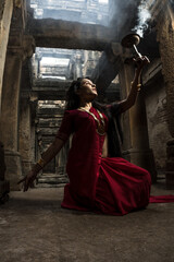 beautiful Indian girl in old stepwell wearing traditional Indian red saree, gold jewellery and...