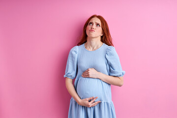 woman is tired to be pregnant, young female in blue dress stand posing isolated on pink background