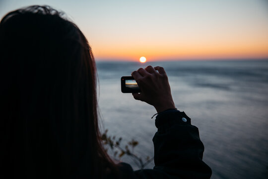 Female filmmaker, taking pictures of sea at sunset