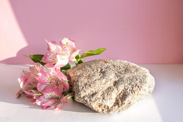 Natural stone stand with flowers for presentation and exhibitions on pink background. Abstract trendy podium for organic cosmetic products. Minimal style.