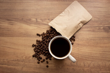 Coffee beans pouring from brown paper bag and coffee in a mug, on wooden table. top view, copy for your text. 
