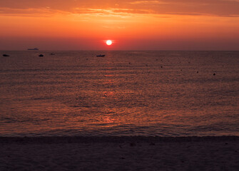 Dark red sunrise with orange sun raising up from the sea with clouds and boat silhoutte at beach Spiaggia di Santa Maria Navarrese, Sardinia, Italy