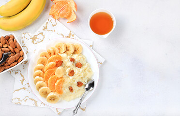 Useful breakfast with ingredients, flat lay, rice pudding with bananas, honey, tangerines and almonds on a sunny table. Healthy and natural food concept, lifestyle, food for children,