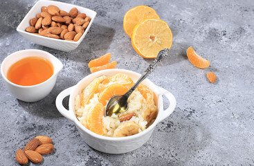 Useful breakfast with ingredients, flat lay, rice pudding with bananas, honey, tangerines and almonds on a sunny table. Healthy and natural food concept, lifestyle, food for children,