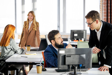male director gives directions and advice to his employee working at the computer in the office, successful team have talk