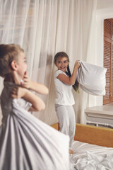 Fototapeta premium Happy little kids in pajamas staged a pillow fight in bed in the bedroom, healthy sleeping, invest in rest concept