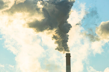 Stream of dark smoke from the chimney of factory in the industrial district. Industrial site with...